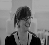 A black and white headshot of a smiling woman in glasses
