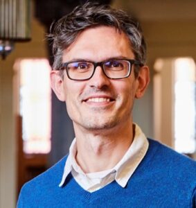 A smiling man in glasses with short dark hair